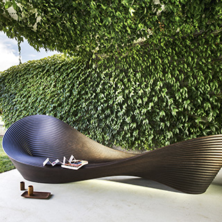 Banco de design de polietileno marrom, visto de frente, em uma area externa.