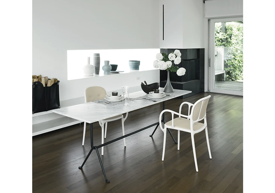 Duas cadeiras empilhaveis assinadas, com estrutura de polipropileno e fibras de vidro, com pintura acetinada ,a cor branca, vista uma de frente para a outra em uma sala de jantar.