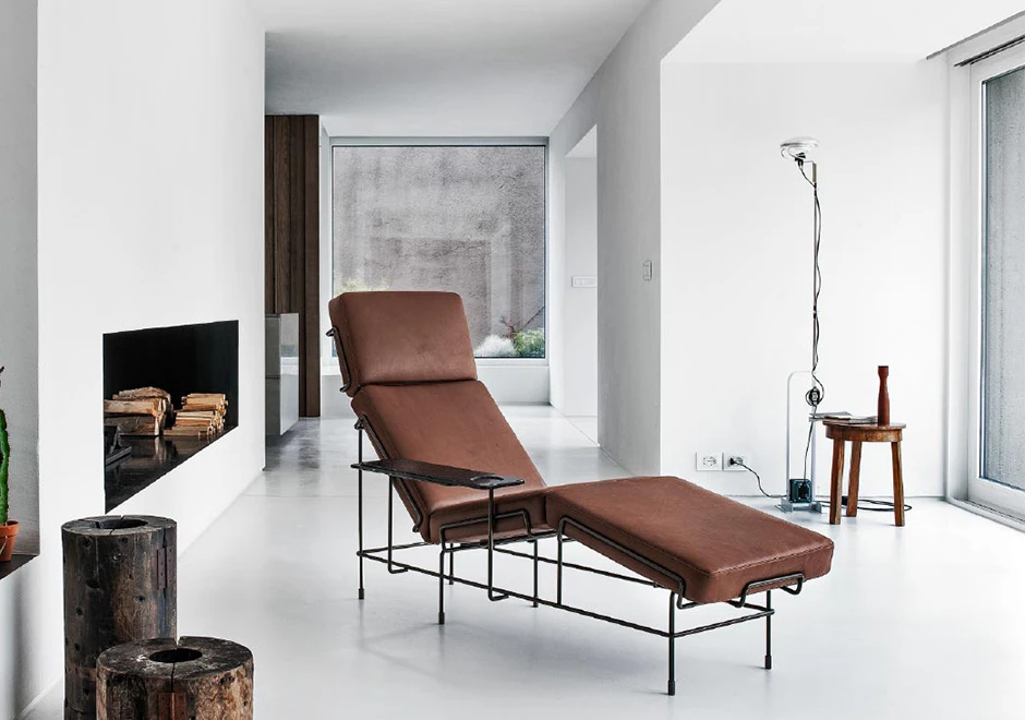 Chaise-longue com estrutura tubular de aço com pintura eletrostática, almofada de assento de poliuretano expandido e capa removível de couro marrom, visto levemente de lado em uma sala moderna.