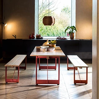 Dois bancos de madeira com estrutura de ferro fundido e assento em Carvalho, com uma mesa ao centro, visto de lado em um ambiente decorado