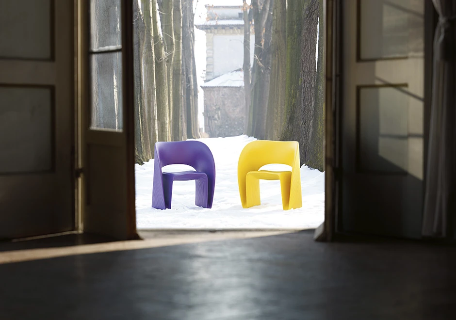 Duas cadeiras de design com estrutura de polietileno roxo e amarelo, uma em frente a outra, em uma area externa.