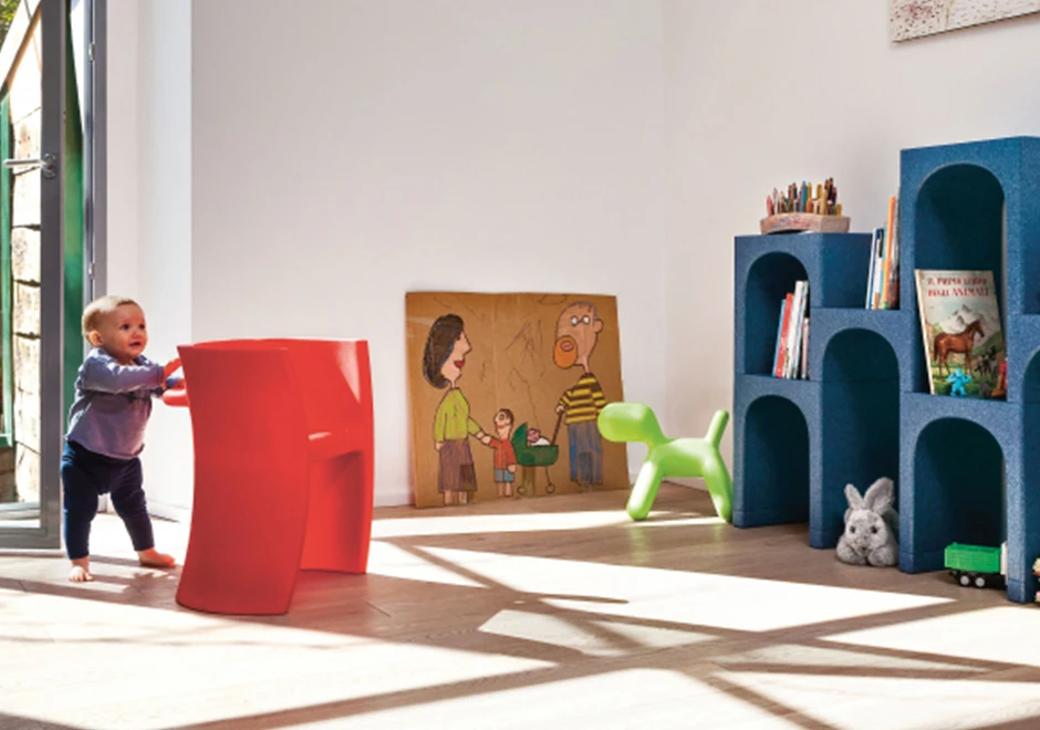 Banco de design em formato de cachorro em polietileno verde, visto de lado, em uma area de recreação infantil.