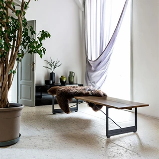 Banco de madeira com estrutura de ferro fundido e assento em Carvalho, com uma pelagem em cima, visto de lado em uma sala moderna.