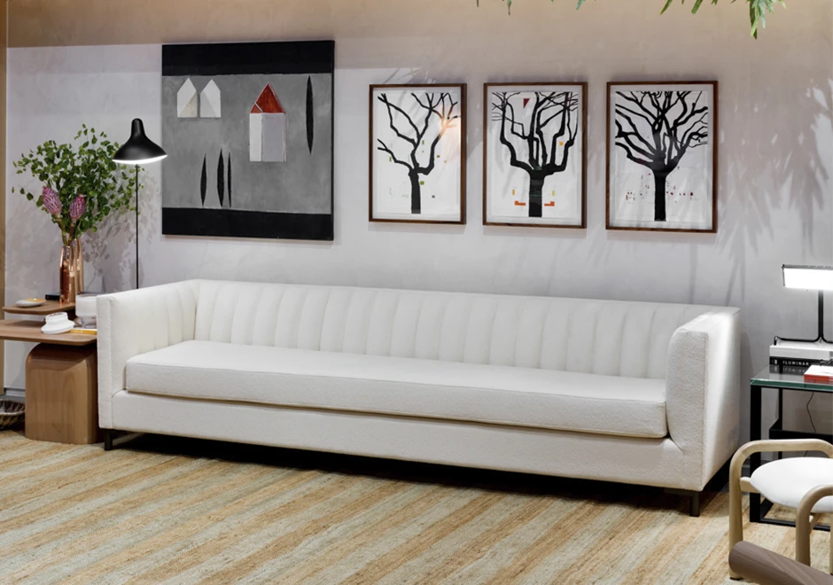 Sofá de design em ondas, com estrutura de madeira, pés em metal, estofado em tecido branco, visto de lado, em uma sala moderna.