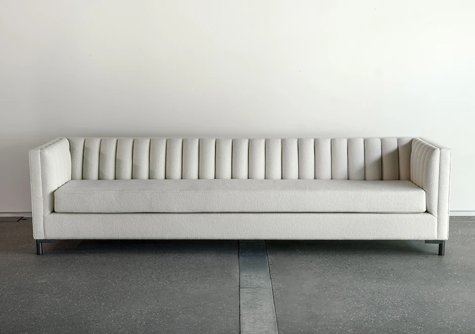 Sofá de design em ondas, com estrutura de madeira, pés em metal, estofado em tecido branco, visto de frente , em um fundo cinza.