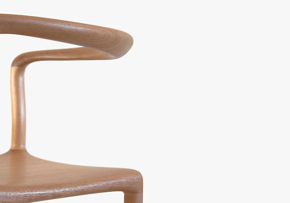 Detalhe de cadeira tripé de madeira Tauari natural, visto de lado, em um fundo branco.