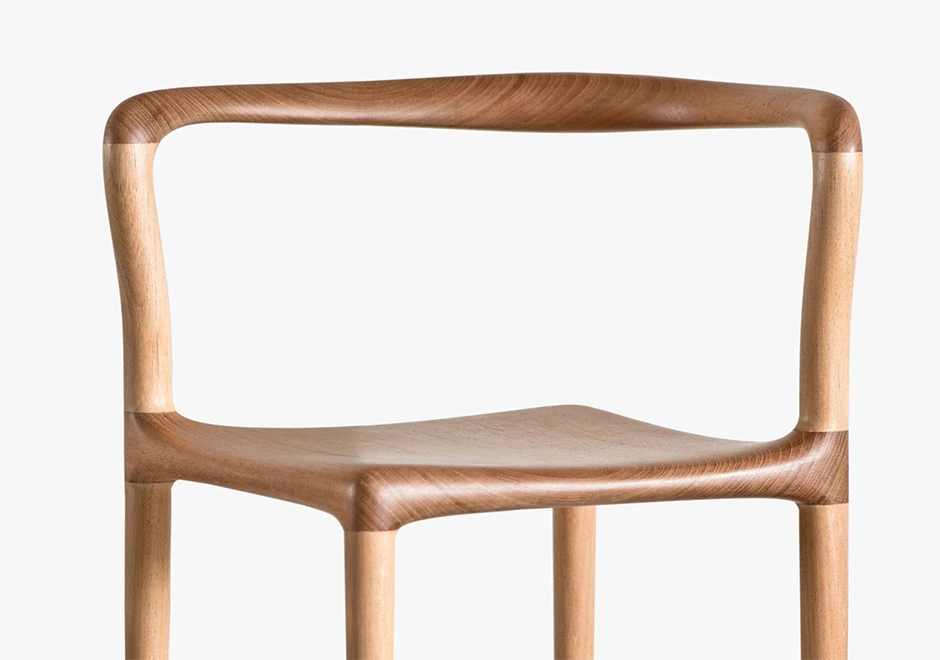 Detalhe de cadeira tripé de madeira Tauari natural, visto de frente, em um fundo branco.