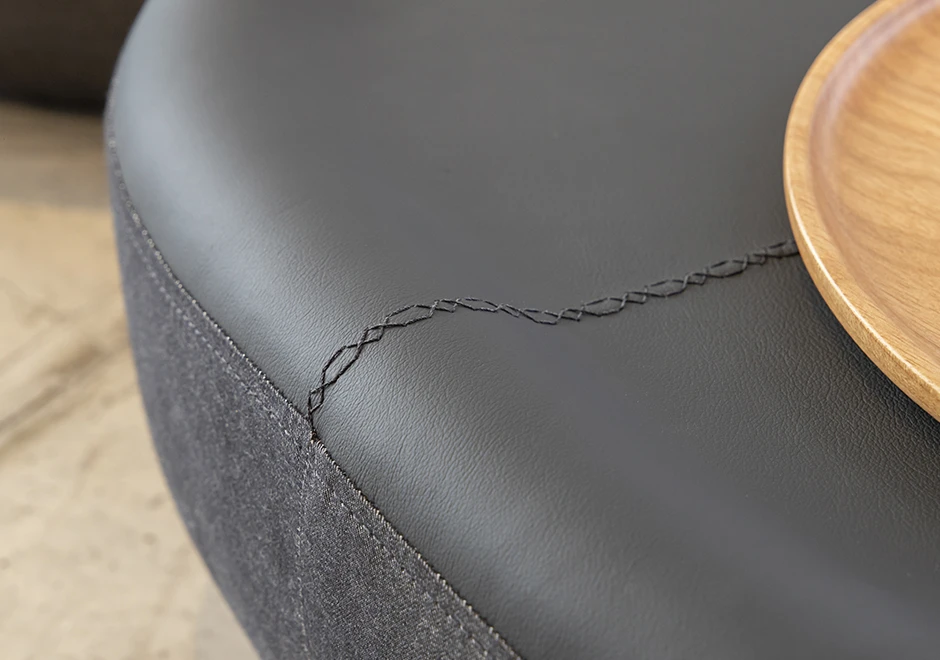 Detalhe de costura de pufes com estrutura de madeira, 3 opções de formato e acabamentos diferenciados em tecido e/ou couro cinza, vistos de cima em um fundo branco.