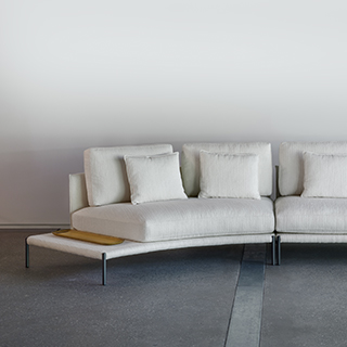 Sofá com escosto com pés de ferro, na cor branca, visto de frente com uma parede branca ao fundo.