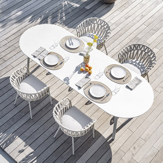 Quatro cadeiras assinadas com estrutura de alumínio com pintura eletrostática; encosto com fita em tecido impermeável trançada à mão. Almofada de assento estofada em tecido branco, visto de cima em uma area externa.