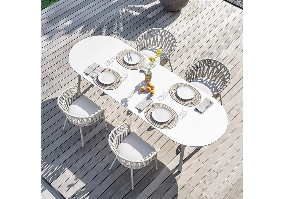 Quatro cadeiras assinadas com estrutura de alumínio com pintura eletrostática; encosto com fita em tecido impermeável trançada à mão. Almofada de assento estofada em tecido branco, visto de cima em uma area externa.