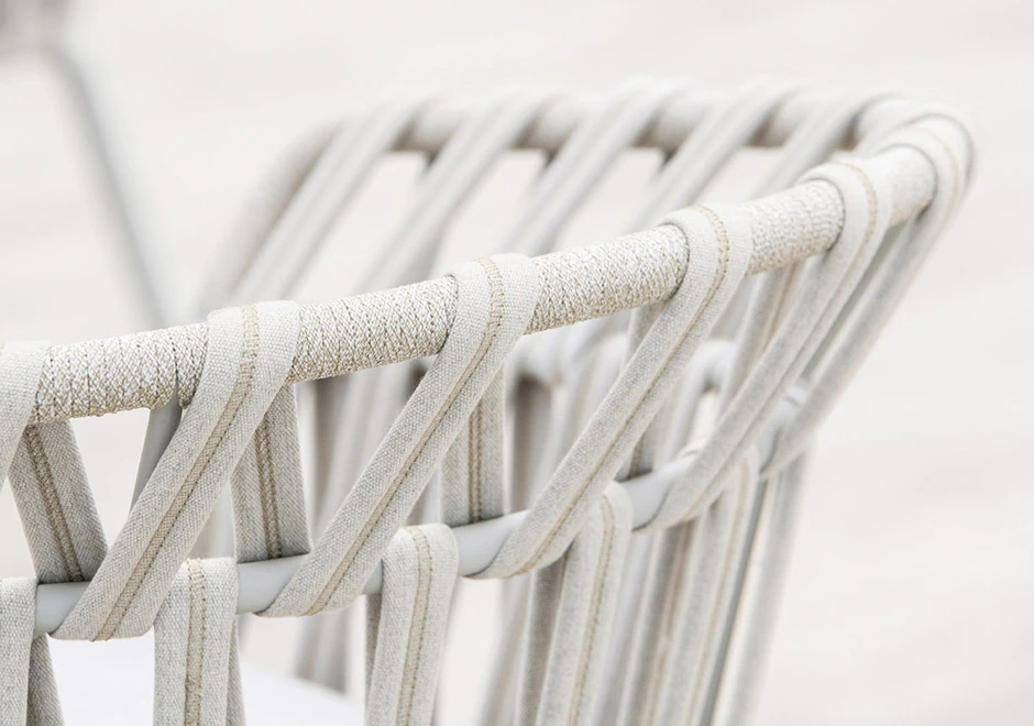 Detalhes de cadeira assinada com estrutura de alumínio com pintura eletrostática; encosto com fita em tecido impermeável trançada à mão. Almofada de assento estofada em tecido branco.