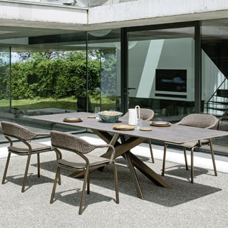 Quatro cadeiras de design com estrutura de alumínio e encosto de fibra sintética trançada a mão na cor bege, em volta de uma mesa, visto de lado, em uma area externa.