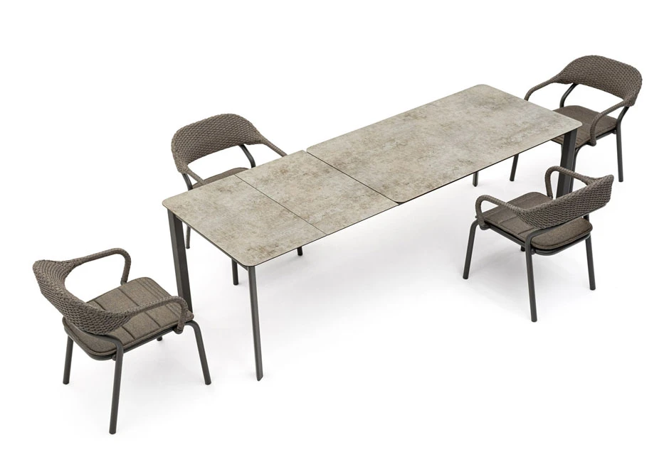 Quatro cadeiras de design com estrutura de alumínio e encosto de fibra sintética trançada a mão na cor bege, em volta de uma mesa em um fundo branco.