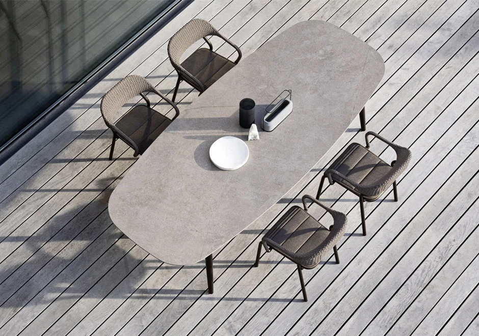 Quatro cadeiras de design com estrutura de alumínio e encosto de fibra sintética trançada a mão na cor bege, em volta de uma mesa, visto de cima, em uma area externa.