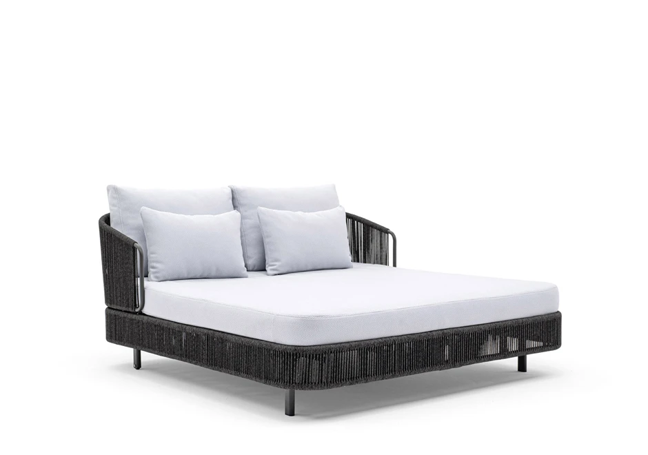 Chaise-longue com estrutura de alumínio com pintura eletrostática, revestida com fibras sintéticas trançadas à mão, dois pés com rodinhas e estofado com espuma branca, visto de lado em um fundo branco.