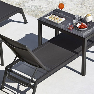 Chaise longue com estrutura de alumínio, assento e encosto em PVC preto, visto de costas em uma area externa.