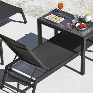 Chaise longue com estrutura de alumínio, assento e encosto em PVC preto, visto de costas em uma area externa.