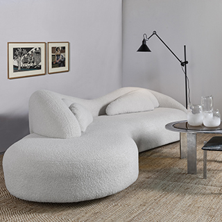 Sofá curvado, branco e com almofadas brancas, também curvadas, visto de lado, em uma sala contemporânea.