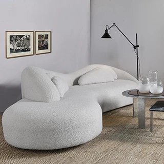 Sofá curvado, branco e com almofadas brancas, também curvadas, visto de lado, em uma sala contemporânea.