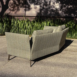 Sofá de design clássico, com estrutura de metal e estofado em tecido verde, visto de lado, em uma area externa.