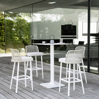 Quatro bancos de design, com estrutura em alumínio com pintura branca. Assento revestido em tecido e encosto com estrutura de alumínio com acabamento em corda trançada à mão, branco, ao redor de uma mesa em uma area externa.