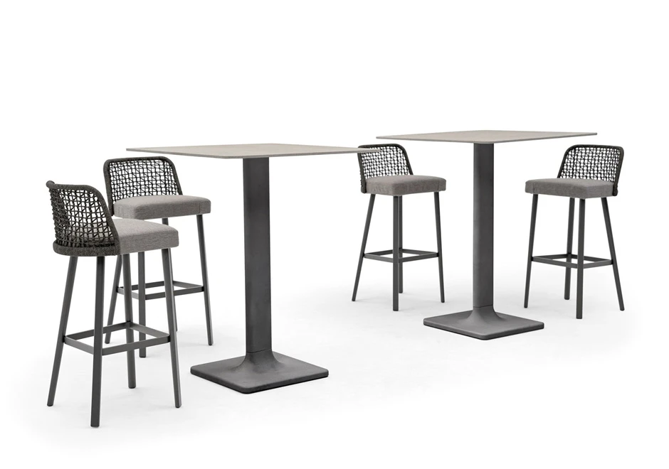 Quatro bancos de design, com estrutura em alumínio com pintura cinza. Assento revestido em tecido e encosto com estrutura de alumínio com acabamento em corda trançada à mão, cinza, ao redor de duas mesas em um fundo branco.