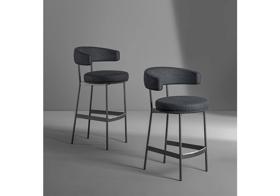 Duas banquetas de bar com estrutura tubular de aço com acabamento em pintura eletrostática, encosto revestido em espuma de poliuretano e assento revestido em espuma de alta-densidade cinza, visto de lado em um fundo branco.