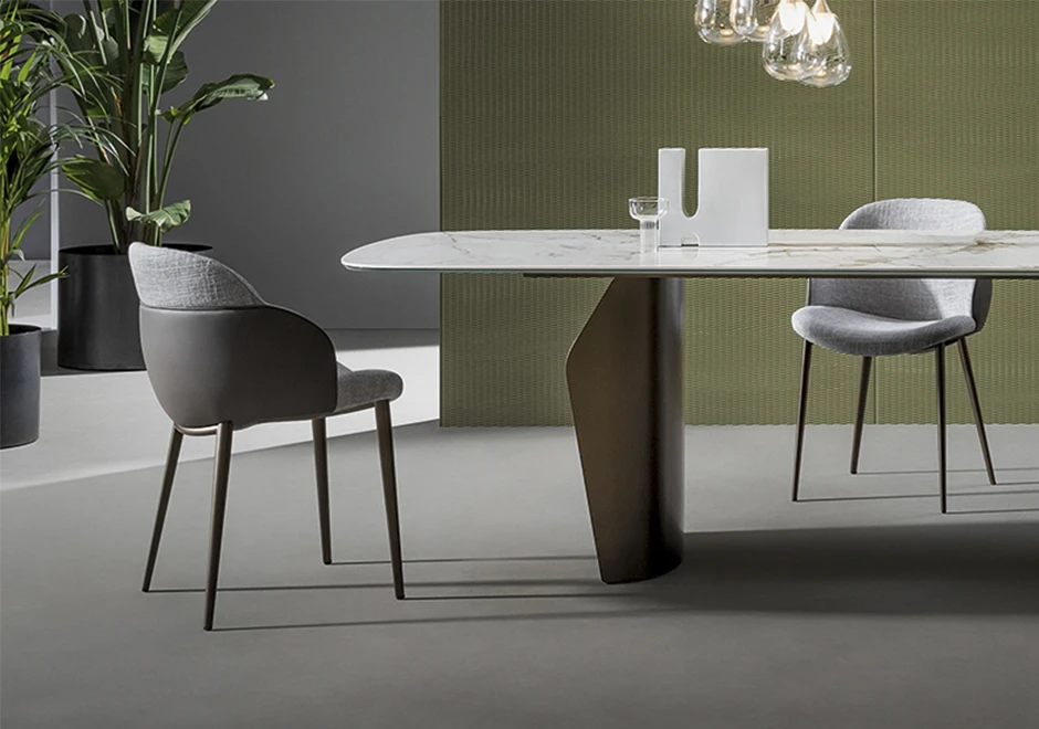 Duas cadeiras de design com estrutura de aço com pintura eletrostática e acabamento em madeira e estofada em tecido cinza, vistas de lado em uma sala com uma mesa de jantar.