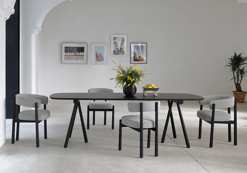 Seis cadeiras assinadas com estrutura freixo maciço tingido de preto e assento e encosto estofados em tecido cinza, em volta de uma mesa de madeira preta, em uma sala moderna.