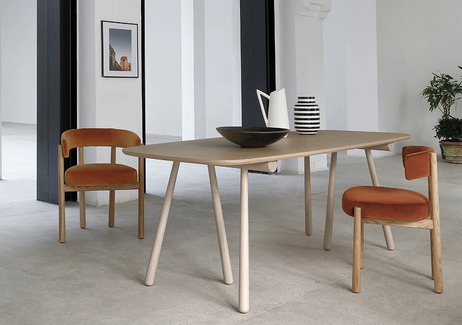 Duas cadeiras assinadas com estrutura em Carvalho maciço natural e assento e encosto estofados em tecido laranja, em volta de uma mesa de madeira bege, em uma sala moderna.