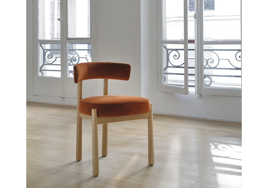 Uma cadeira assinada com estrutura em Carvalho maciço natural e assento e encosto estofados em tecido laranja, em uma sala vazio, vista de frente.