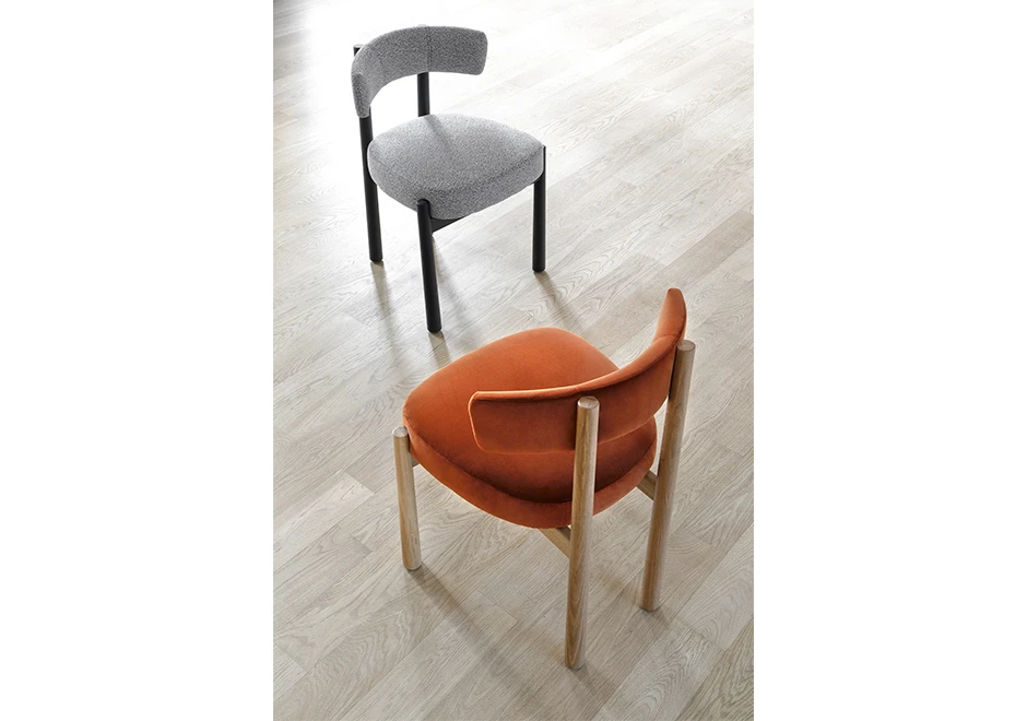 Duas cadeiras assinadas, uma com estrutura em Carvalho maciço natural e assento e encosto estofados em tecido laranja, e outra com estrutura freixo maciço tingido de preto e ssento e encosto estofados em tecido cinza, uma de frente para outra.