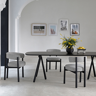 Três cadeiras assinadas com estrutura freixo maciço tingido de preto e assento e encosto estofados em tecido cinza, em volta de uma mesa de madeira preta, em uma sala moderna.