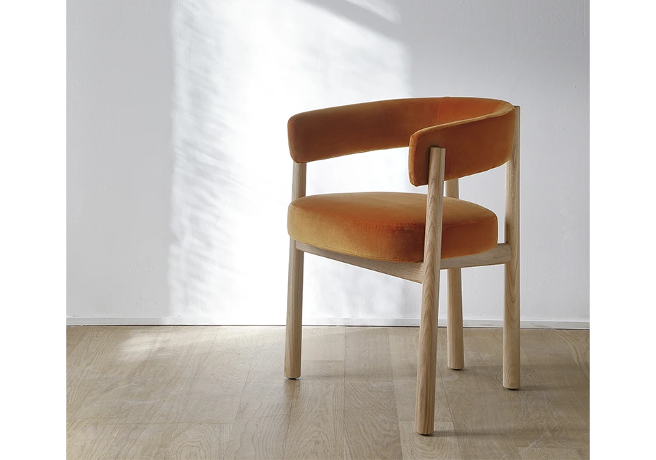 Uma cadeira assinada com estrutura em Carvalho maciço natural e assento e encosto estofados em tecido laranja, em uma sala vazia, vista de lado