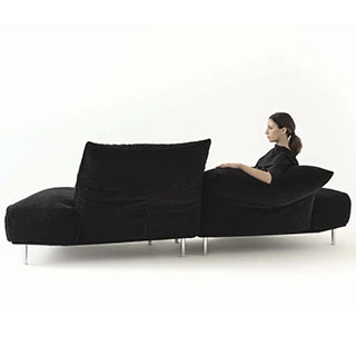 Sofá modular estofado em tecido cinza, visto de costas, com uma pessoa sentada, em um fundo branco.