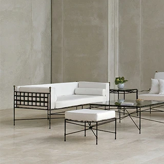 Sofá contemporâneo, cadeira e um banquinho com assentos e encostos brancos, almofadas brancas e estrutura fina e escura em um cenário cinza com duas mesas com tampos de vidro.