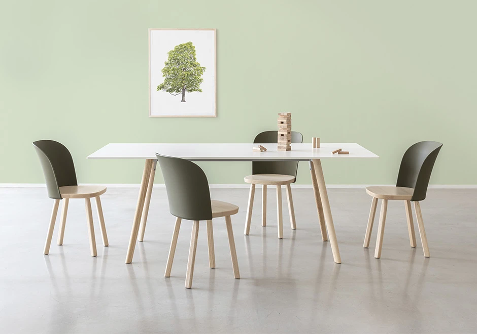 quatro cadeiras assinadas de madeira e uma mesa de jantar de madeira com uma torre jenga sobre ela. Quadro de árvore ao fundo.