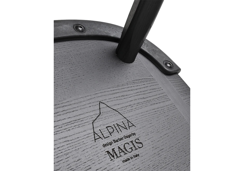 detalhe da parte de baixo do assento de uma cadeira assinada de madeira preta, onde se lê a marca ALPINA MAGIS e se vê uma pequena parte de um dos pés.