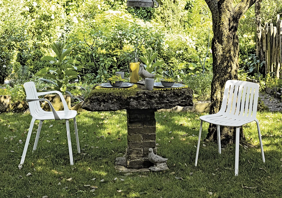 Duas cadeiras empilhaveis, com estrutura de alumínio pintado em poliéster na cor branco, em volta de uma mesa, em uma area externa.