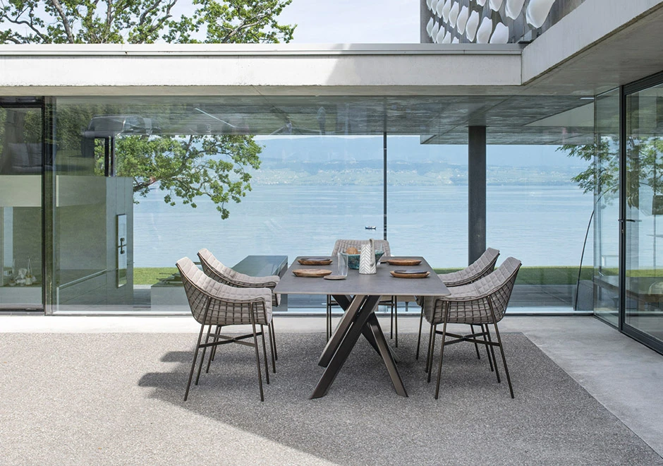 Cadeiras de design com estrutura de aço cromado preto e tecido branco, vista de lado, em uma area externa em volta de uma mesa.