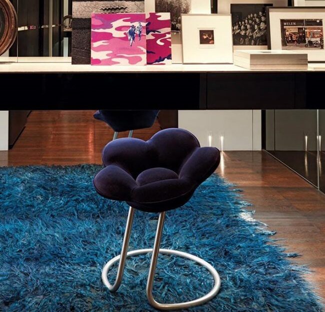 Banco de design com estrutura de metal pintado de cinza metálico e assento de veludo azul, visto de lado em uma sala moderna.