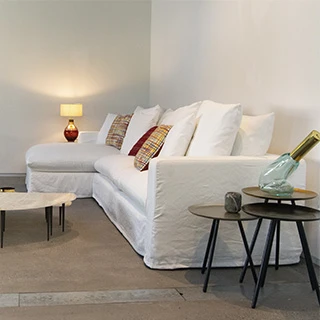 Sofá modular estofado em tecido branco e almofadas decorativas, visto de lado em uma sala de parede branca.