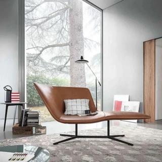 Chaise-longue com estrutura de aço com acabamento bronze, revestida em espuma moldada em diferentes densidades, estofada em couro marrom, visto de lado em uma sala moderna.