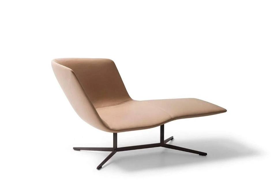 Chaise-longue com estrutura de aço com acabamento bronze, revestida em espuma moldada em diferentes densidades, estofada em couro bege, visto de lado em um fundo branco.