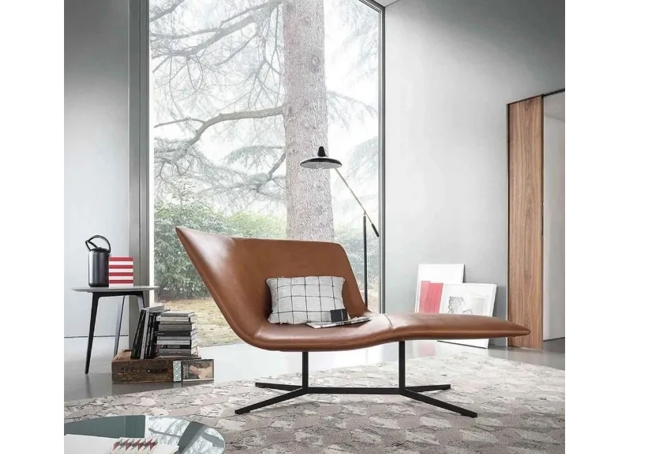 Chaise-longue com estrutura de aço com acabamento bronze, revestida em espuma moldada em diferentes densidades, estofada em couro marrom, visto de lado em uma sala moderna.