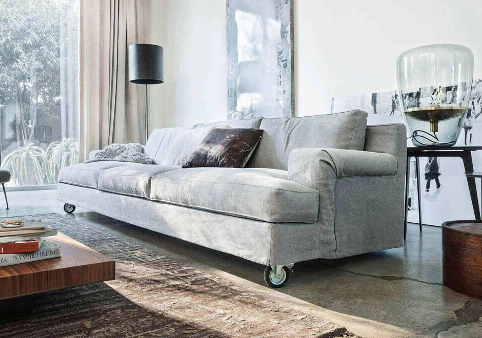 sofá aconchegante de três lugares com uma almofada, um abajur de cada lado, fotos ao fundo e uma cortina do lado esquerdo.