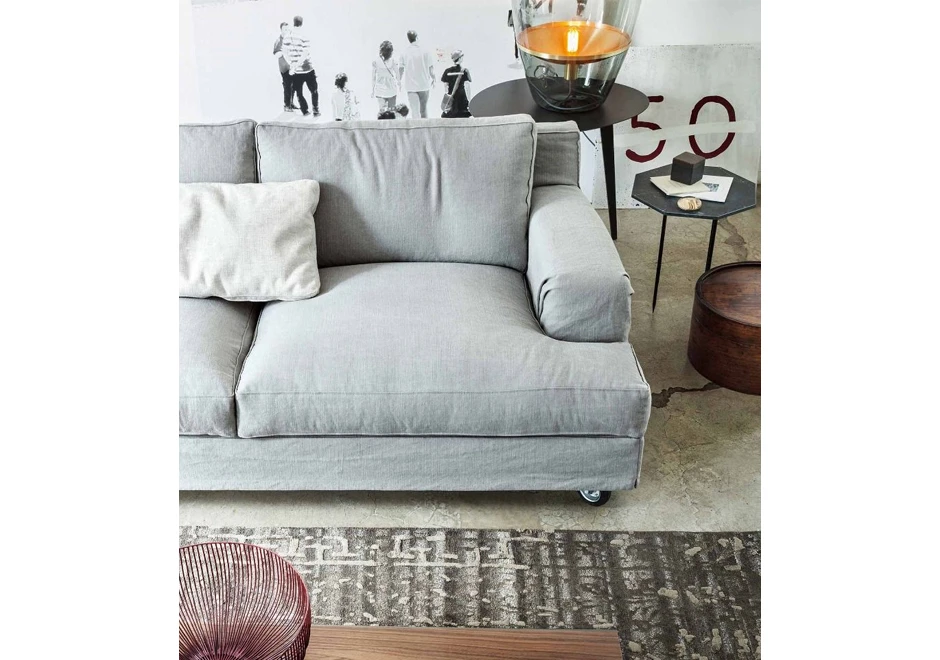 metade de um sofá aconchegante, com uma almofada, uma mesinha ao lado, um abajur e uma foto ao fundo e parte de um tapete embaixo.