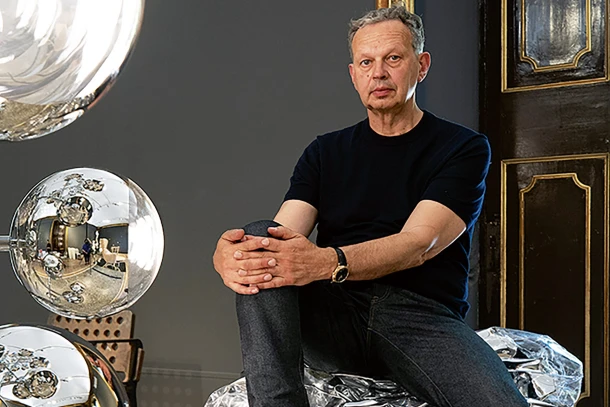 Tom dixon veste preto e jeans, sentado próximo a uma de suas criações.