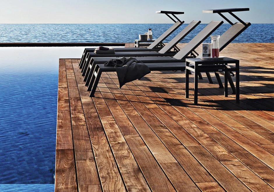 Quatro chaise longue com estrutura de alumínio, assento e encosto em PVC preto, visto de lado em uma area externa.